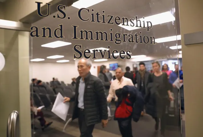USCIS logo on door of room with people in ine
