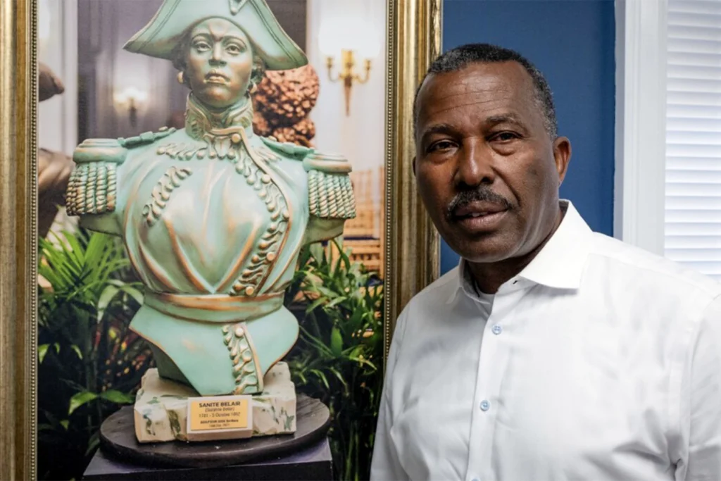 Norwalk Realtor Guy Bocicaut stands next to a photo featuring a bust of Haitian revolutionary leader Sanité Bélair